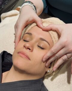 Picture of the face of a female client lying down on a massage table, while the professional is performing a facial service